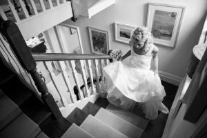 a black and white photograph of a bride coming up the stairs in her wedding gown
